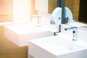 lavabo in ceramica bianca e rubinetto dell'acqua con dosatore di sapone in bagno o toilette foto