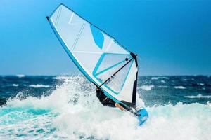 windsurfer che cavalca le onde durante le vacanze con una vela bianca sull'acqua blu dell'Oceano Atlantico foto