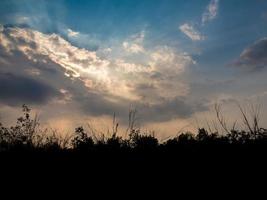 silhouette alberi e raggio di sole dietro nuvole scure in campagna foto