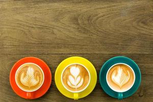 vista dall'alto di 3 caffè latte o cappuccino in tazza giallo arancio e blu scuro con latte art foto