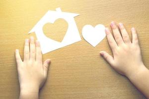 mani dei bambini con piccolo modello di casa e cuore su fondo di legno foto