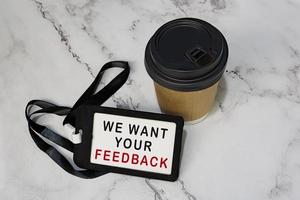 vogliamo il tuo feedback sull'etichetta nera con la tazza di caffè usa e getta sulla scrivania bianca foto