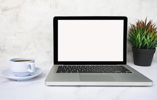 laptop o notebook con schermo vuoto, caffè e pianta in vaso sul tavolo bianco. foto