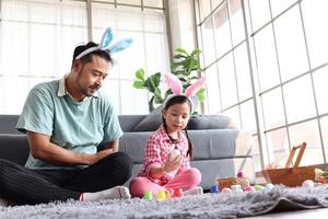 padre figlia che prepara bellissime uova di Pasqua per la decorazione e la celebrazione dell'inizio della primavera, adorabile coniglietta rosa bambino e suo padre con le orecchie di coniglio fascia per la testa dipingono insieme uova colorate foto