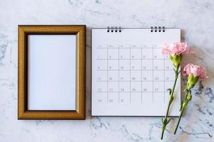 fiore di garofano su cornice vuota e calendario su sfondo marmo, San Valentino, festa della mamma o sfondo di compleanno foto