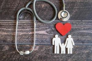 cuore rosso, stetoscopio e famiglia di icone sulla scrivania di legno. concetto di assicurazione medica foto
