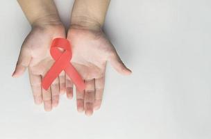 mani del bambino che tengono il nastro rosso per la consapevolezza dell'aids. aiuta la consapevolezza foto