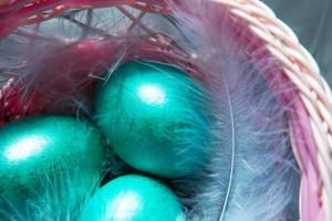 uova di pasqua lucide in marmo colorato dipinto in un cesto con piume delicate primo piano. nido con paglia - decorazione pasquale sul tavolo foto