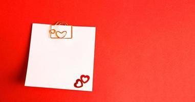 foglio quadrato per appunti con graffetta a forma di lettera e cuore. decorazione di coppie innamorate di cuori su sfondo rosso. san valentino, messaggio, saluto, dichiarazione d'amore. copia spazio foto