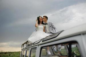 gli sposi hipster sono in piedi vicino al loro autobus retrò. foto