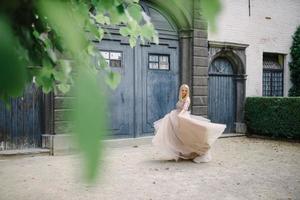 giovane bella donna bionda in splendido abito lungo blu che cammina per la strada vicino al vecchio edificio nella città vecchia. foto