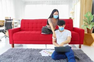 giovane coppia che indossa una maschera facciale che lavora da casa durante la quarantena da coronavirus o pandemia covid-19 come nuova politica normale implementata