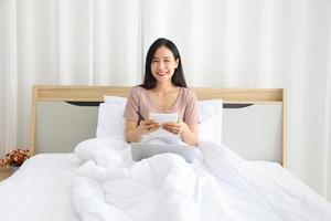donna asiatica che lavora online da casa con il laptop sul letto per una nuova vita normale durante il periodo di quarantena da covid-19 foto
