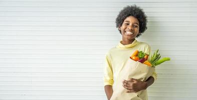 bambino sano felice, ragazzino adorabile che sorride e tiene in mano un sacchetto di carta con cibo fresco pieno di verdure nello spazio della copia foto