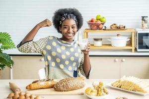 giovane donna felice afro-americano capelli afro facendo forte mano mentre beve un latte per colazione con divertimento foto