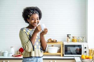 giovane donna felice capelli afro afroamericani che bevono caffè in cucina al mattino. foto