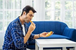 un allegro giovane padre attraente è seduto a casa sul divano e mangia la pizza nel comodo divano del soggiorno foto