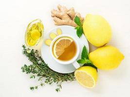 modi popolari per curare il raffreddore - tazza di tè e una fetta di limone, zenzero, menta, miele, erbe aromatiche, limoni interi e metà su sfondo bianco, vista dall'alto. foto