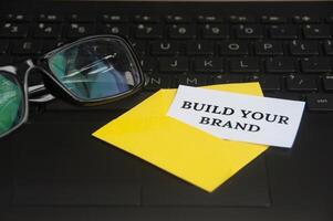 costruisci il testo del tuo marchio su un piccolo pezzo di carta in una busta con lo sfondo del laptop. foto