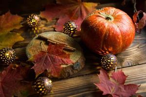 zucca rotonda naturale arancione su un tavolo di legno con foglie d'acero gialle e rosse cadute, bastoncini di cannella. ghirlande di luci, calda atmosfera autunnale, ringraziamento, festa del raccolto, halloween. copia spazio foto