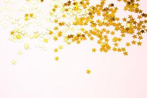 paillettes dorate a forma di stelle brillano su uno sfondo rosa. sfondi con copyspace per vacanze, decorazioni per feste, natale e capodanno, compleanno e anniversario. gradiente e consistenza foto