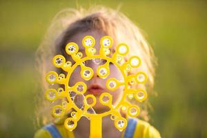 una ragazza con una tuta di jeans soffia bolle di sapone in estate in un campo al tramonto. giornata internazionale dei bambini, bambino felice, attività all'aperto. sfondo estivo. stile di vita sano ed ecologico foto