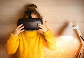 una ragazza con gli occhiali per realtà virtuale si siede vicino a una lampada con una luce magica. maglione giallo, tecnologia e sviluppo dei bambini. foto