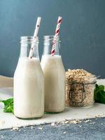 frullato con farina d'avena, menta per una sana colazione. latte d'avena in bottiglia di vetro con tubo su sfondo di pietra scura. foto