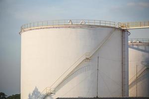 grandi serbatoi industriali per benzina e olio con cielo blu. serbatoi di carburante presso la tank farm. scale di metallo sul lato di un contenitore industriale dell'olio. scala su grande serbatoio carburante foto