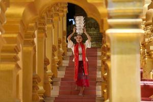 giovane ragazza asiatica in costume tradizionale birmano che tiene una ciotola di riso a portata di mano alla pagoda dorata nel tempio del myanmar. donne del Myanmar che tengono fiori con abiti tradizionali birmani che visitano un tempio buddista foto