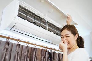 donna asiatica che pulisce un filtro dell'aria condizionata sporco e polveroso nella sua casa. casalinga che rimuove un filtro polveroso del condizionatore d'aria. foto