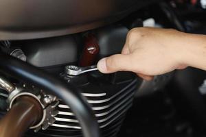 meccanico che utilizza una chiave inglese e una presa sulla testata di una motocicletta .manutenzione, riparazione moto concetto in garage .messa a fuoco selettiva foto