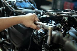 meccanico che utilizza una chiave inglese e una presa sulla testata di una motocicletta .manutenzione, riparazione moto concetto in garage .messa a fuoco selettiva foto