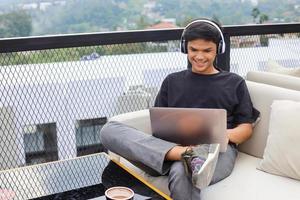 studente maschio asiatico che si rilassa sul divano mentre studia online utilizzando laptop e cuffie foto