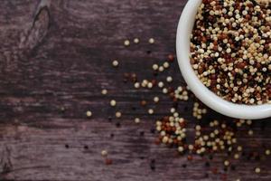 semi di quinoa nella tazza bianca su fondo di legno. la quinoa è una buona fonte di proteine per le persone che seguono una dieta a base vegetale. foto