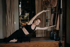 giovane istruttore femminile di pilates che si esercita e si allunga sul riformatore cadillac foto