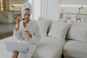 giovane bella donna in accappatoio che applica polvere sul viso mentre fa il trucco quotidiano a casa foto