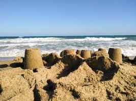 castello di sabbia colpito da un'onda del mare su una spiaggia foto