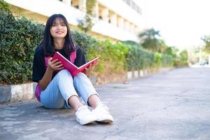 studentessa con zaino rosa seduto a terra con sfondo scolastico. foto