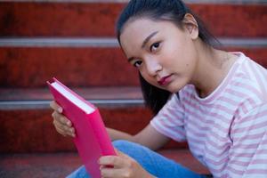 sorriso giovane ragazza tenere libro rosa seduto a scuola, ragazza asiatica. foto
