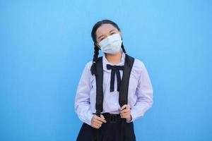 la ragazza della scuola indossa la maschera su sfondo blu, torna a scuola. foto