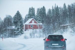 guida in auto nella bufera di neve con casa rossa in campagna in inverno foto