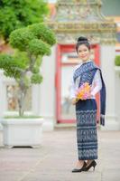 Attraente donna tailandese in un antico abito tailandese tiene un fiore fresco che rende omaggio al buddha per esprimere un desiderio sul tradizionale festival di Songkran in Thailandia foto