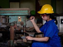 donne asiatiche in uniforme meccanica usano utensili elettrici per perforare barre di metallo in fabbrica foto