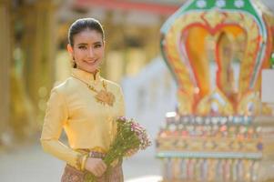 Attraente donna tailandese in un antico abito tailandese tiene un fiore fresco che rende omaggio al buddha per esprimere un desiderio sul tradizionale festival di Songkran in Thailandia foto