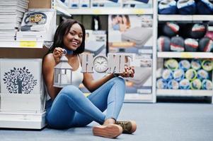 ritratto di una bella donna afroamericana seduta sul pavimento con un cartello di casa e una torcia in mano nel negozio. foto