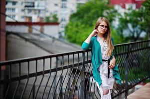 ragazza alla moda con occhiali e jeans strappati contro la barriera sulla strada. foto