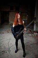 la ragazza punk dai capelli rossi indossa il nero con il basso in un luogo abbandonato. ritratto di musicista donna gotica. foto