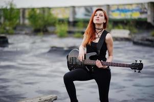 ragazza punk dai capelli rossi indossa su nero con basso sul tetto. foto