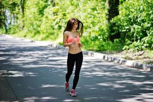 ragazza sportiva fitness in abbigliamento sportivo correre su strada nella foresta con una bottiglia d'acqua a portata di mano, sport all'aria aperta, stile urbano. foto